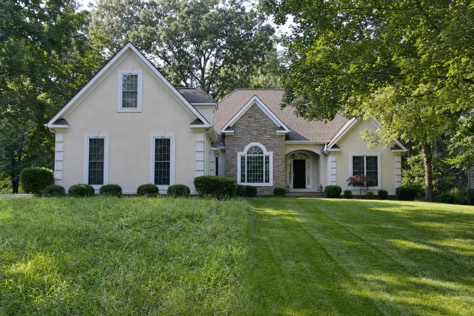 A front lawn with tall grass on the left and a freshly striped cut on the right, in front of the same house